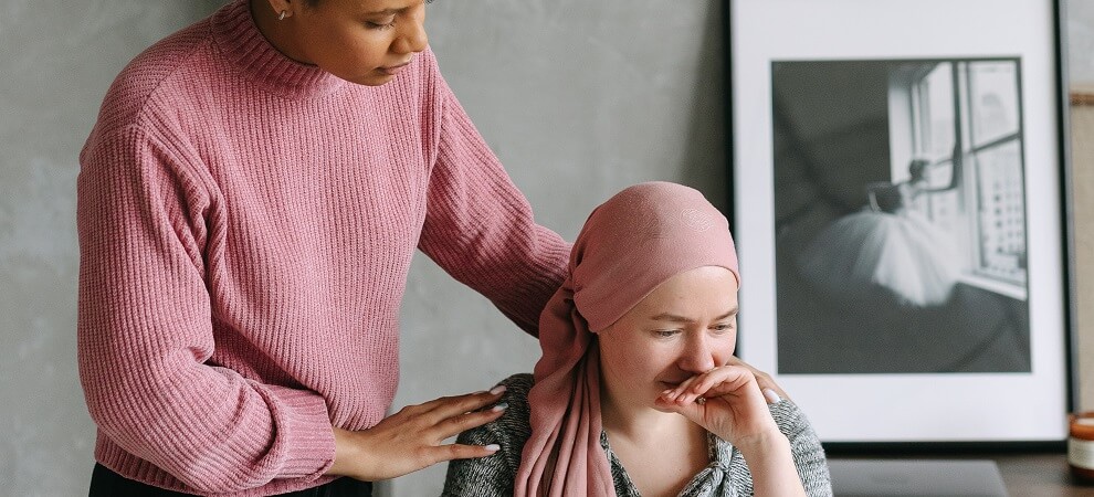 female patient in pink headscarf being consoled by her mesothelioma caregiver